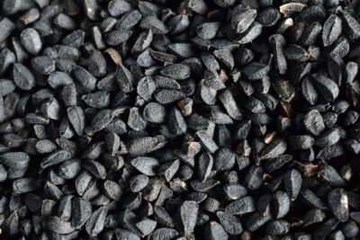 Detailné čierne semienka čiernej rasce (Nigella sativa) jemne rozptýlené na drevenom povrchu, symbolizujúce prírodný zdroj bioaktívnych zlúčenín.